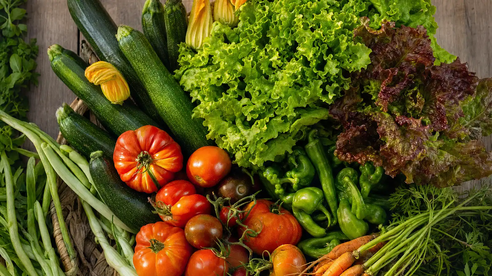 Bodegón de verduras de temporada: calabacines con flor, lechugas, tomates, pimientos, zanahorias y cebolletas