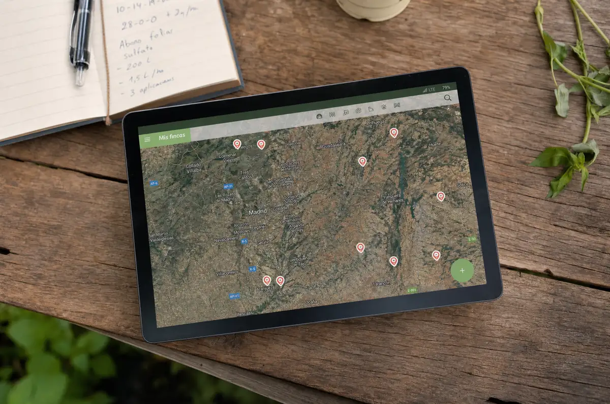 Tablet con mapa de fincas de la red Origen Tu Campo sobre mesa de madera de campo — vista de satélite con pins de productores activos